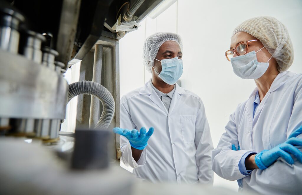 Male Technician Talking to Woman while Inspecting Manufacturing Machine at Pharmaceutical Factory