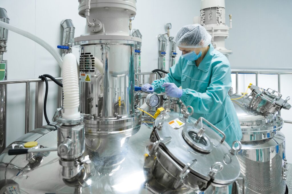 Pharmaceutical factory woman worker in protective clothing operating production line in sterile
